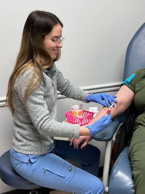 A healthcare worker draws blood from a seated patient’s arm using a needle and vial in a clinical setting, focusing on precise technique and care throughout the process. Learn more about this essential medical procedure.