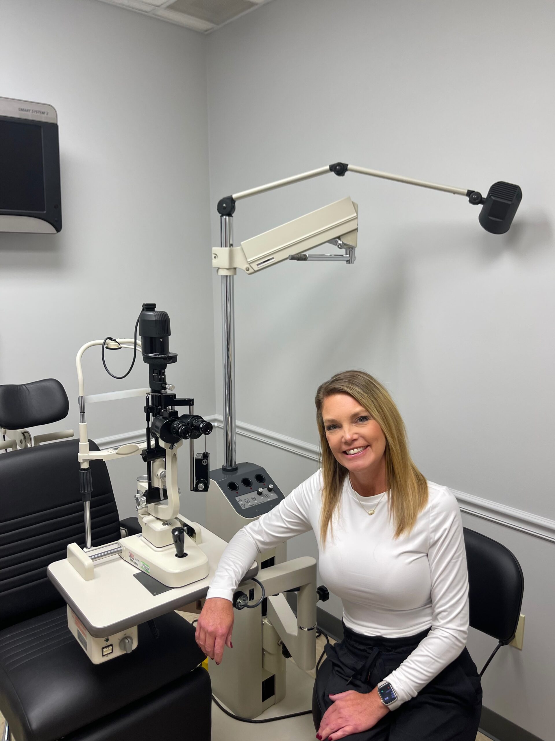 A woman sits next to an ophthalmology exam machine in a clean, modern eye clinic, learning about her eye health.